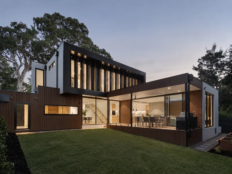 Modern two-story home with timber siding and large windows at dusk